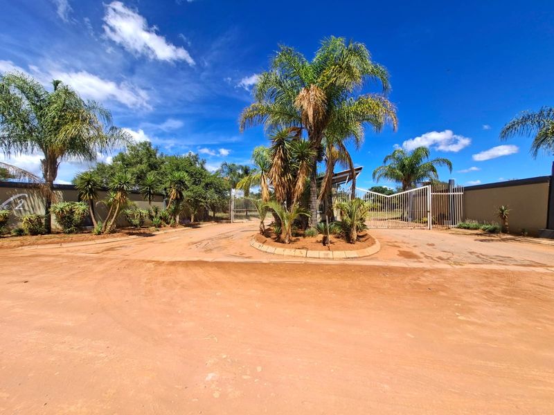 A view of the property entrance featuring a gated access point, perimeter walling, and established palm trees within a landscaped garden island.