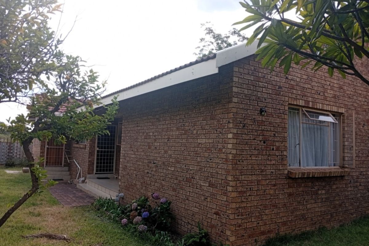 Rear view of a face brick townhouse featuring a tiled roof, security gates, and a paved walkway leading to the entrance.