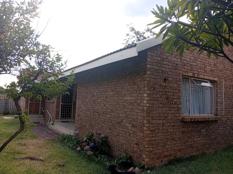 Rear view of a face brick townhouse featuring a tiled roof, security gates, and a paved walkway leading to the entrance.
