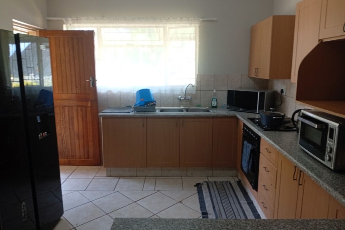 Functional kitchen featuring laminate cabinetry, granite countertops, double basin sink, and built-in oven with hob, finished with tiled flooring and natural light.