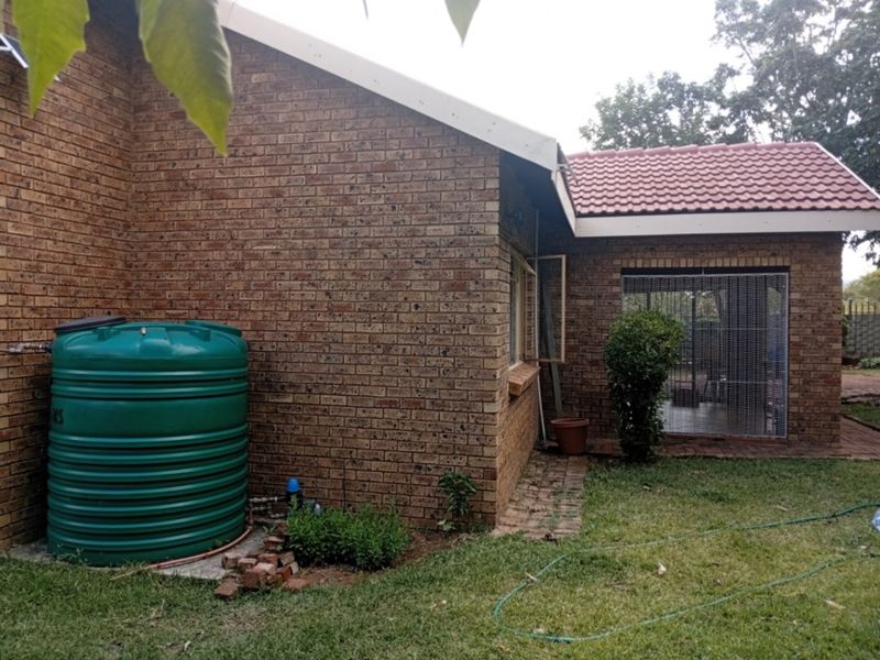 Rear view of the townhouse featuring face brick walls, a tiled roof, and an installed water storage tank in the garden area.