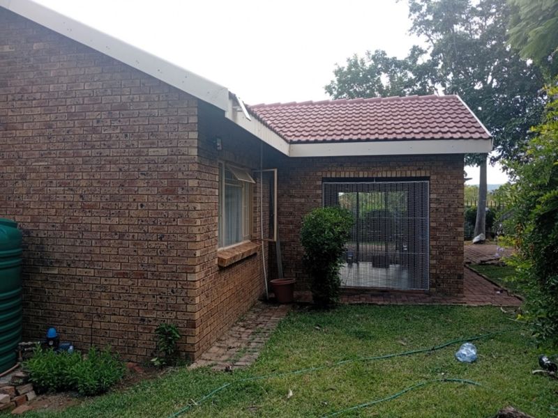 Rear view of a face brick townhouse featuring a tiled roof, security gate, and an integrated water tank in the garden area.