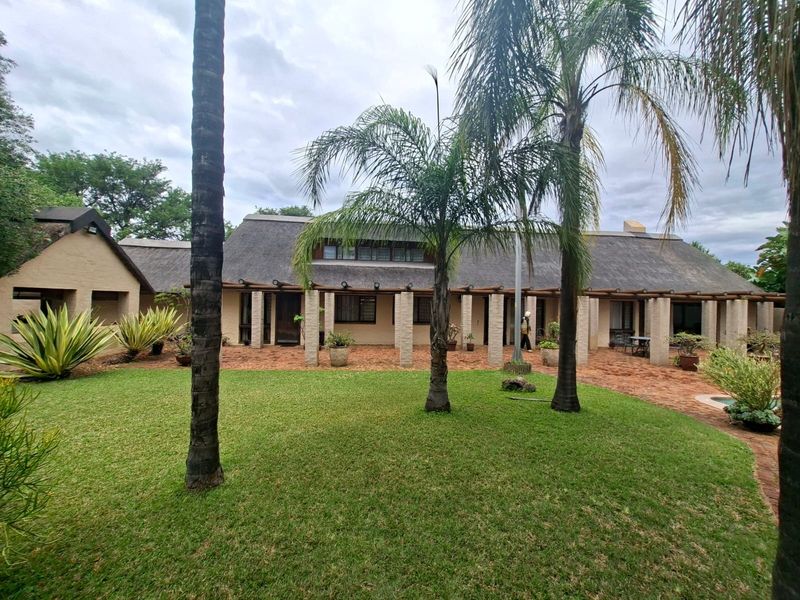 A spacious rear garden featuring a large brick patio, stone pillars, and a traditional thatched roof house exterior.