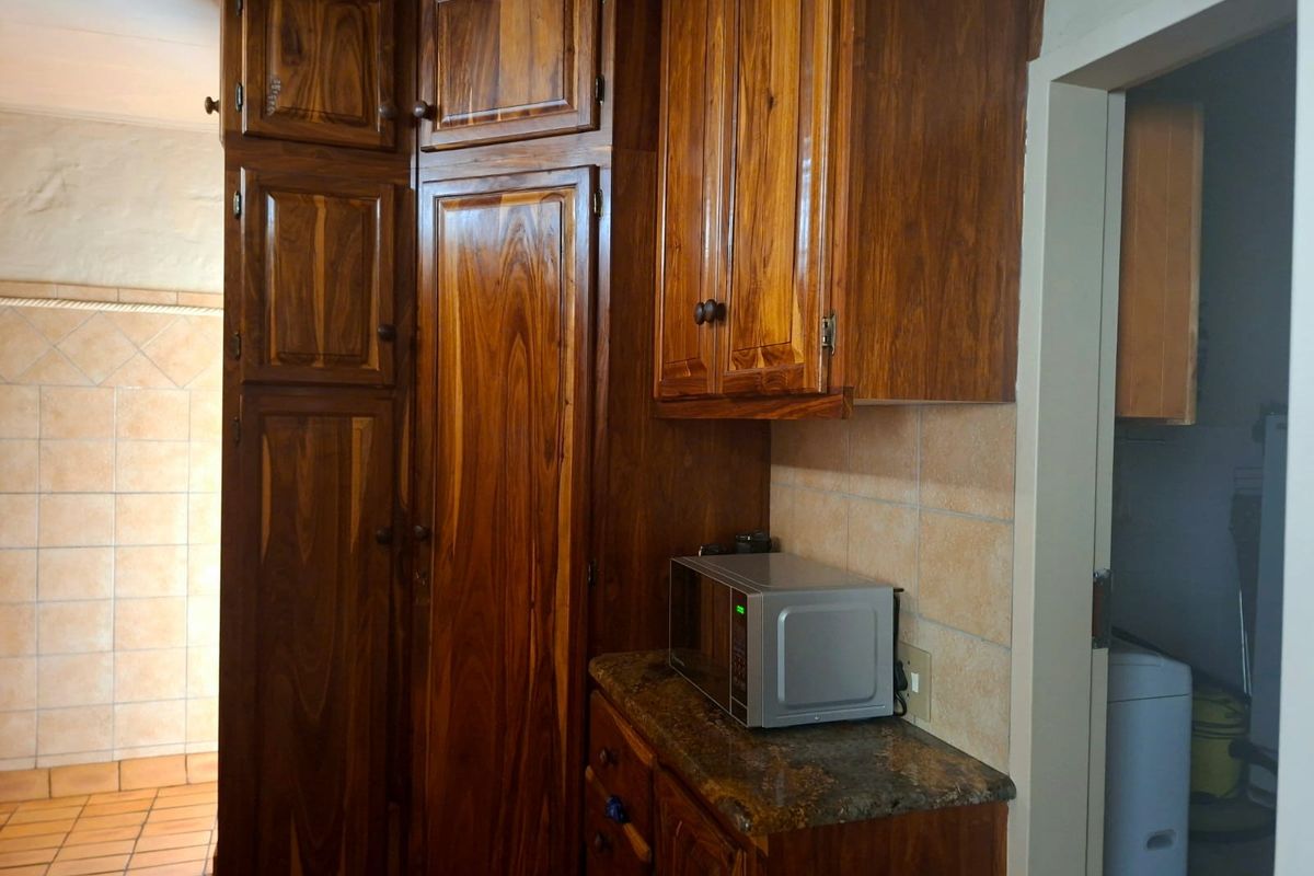A kitchen area featuring traditional wooden cabinetry, stone countertops, and tiled finishes, providing a functional workspace with adjacent utility access.