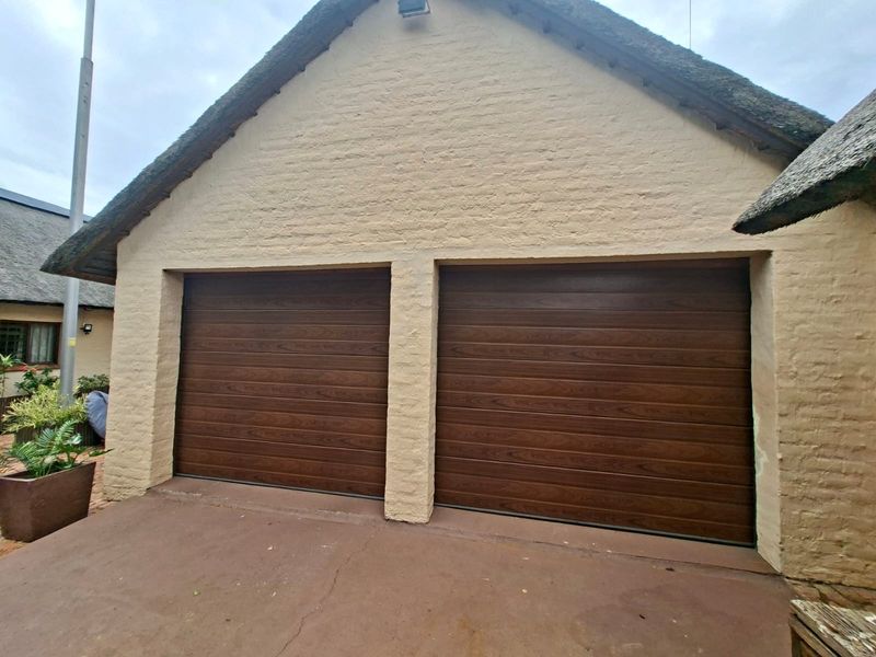 A double garage featuring wood-look sectional doors and a traditional thatched roof, set against a textured brick facade with a concrete driveway.