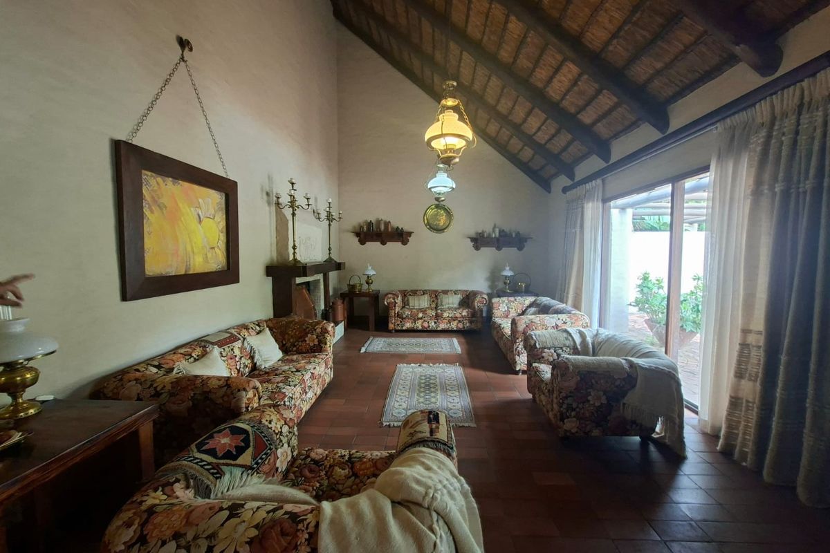 Spacious living room featuring a high vaulted thatched ceiling with exposed timber beams, terracotta flooring, a fireplace, and large sliding doors leading outdoors.