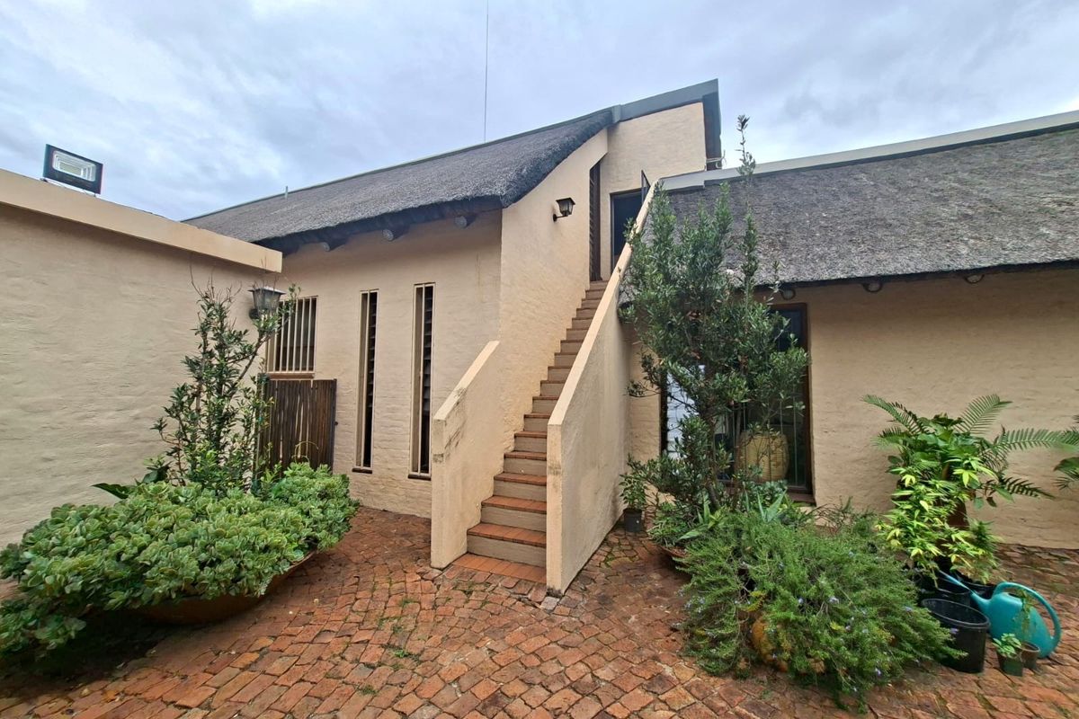 A rear courtyard featuring brick paving, a thatched roof structure, and an external staircase leading to an upper level.