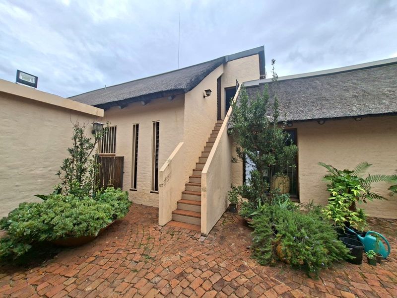 A rear courtyard featuring brick paving, a thatched roof structure, and an external staircase leading to an upper level.