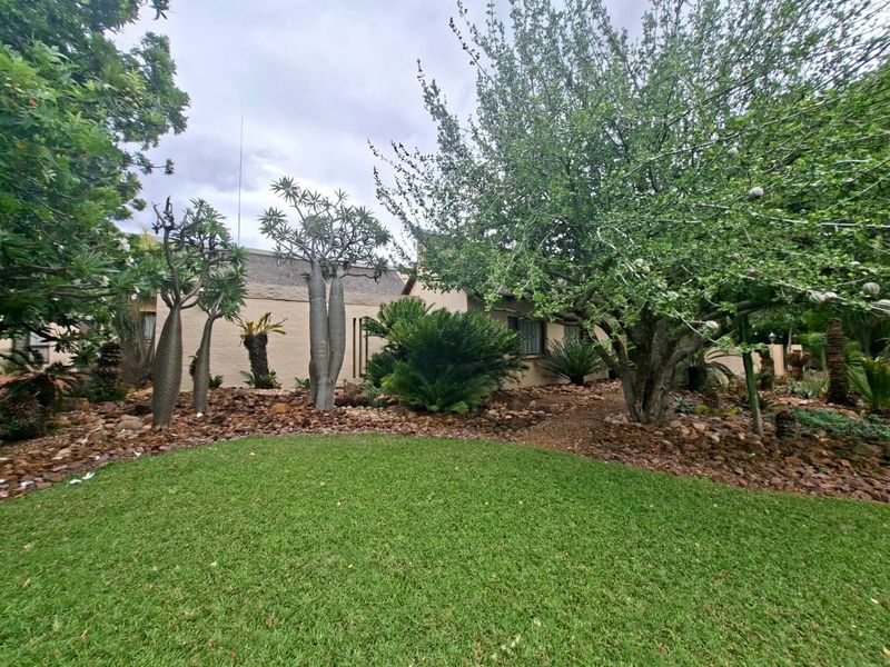 A well-maintained rear garden featuring a lush green lawn, mature trees, and a decorative rockery area adjacent to the house exterior.