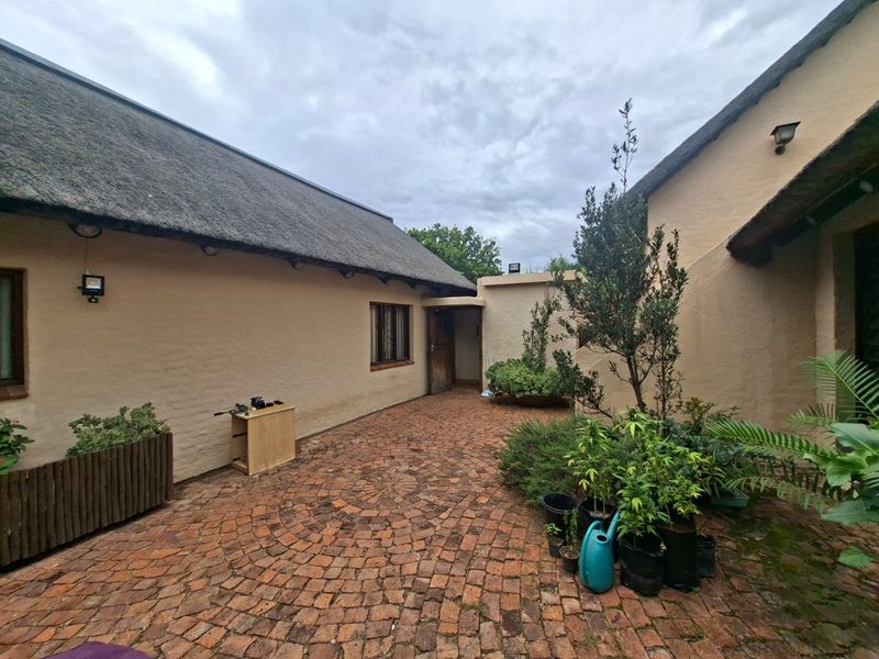 A private courtyard area featuring traditional thatched roofing and rustic brick paving, offering a charming outdoor space between building wings.