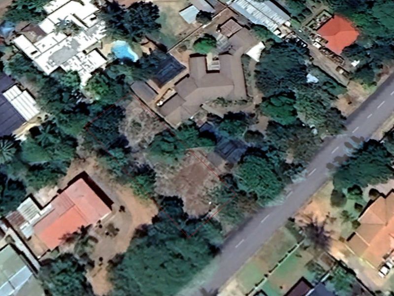 Aerial view of a vacant residential plot featuring mature trees and vegetation, outlined in red within an established suburban neighborhood.
