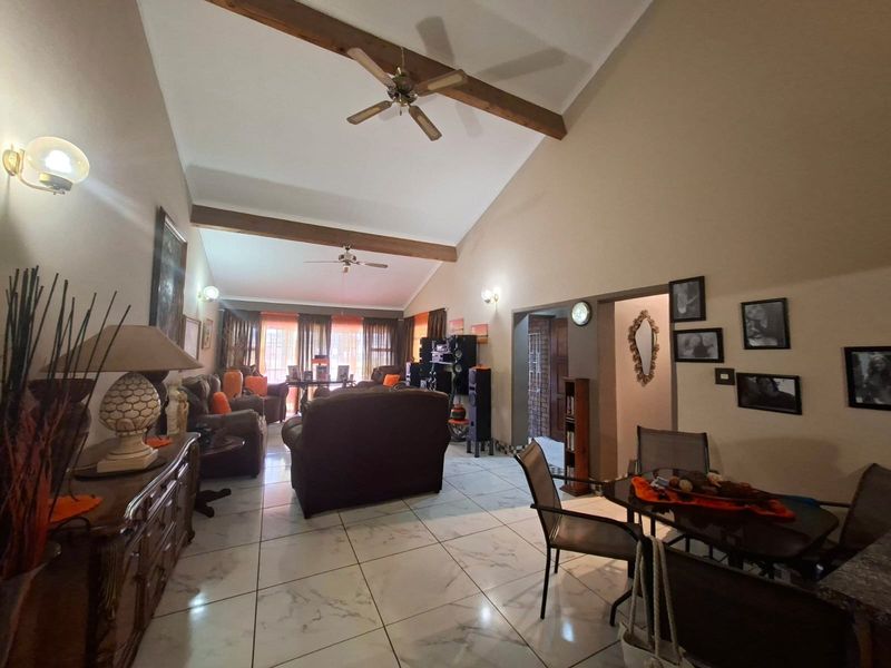 Spacious open-plan living and dining area featuring high vaulted ceilings with exposed timber beams, tiled flooring, and ceiling fans.