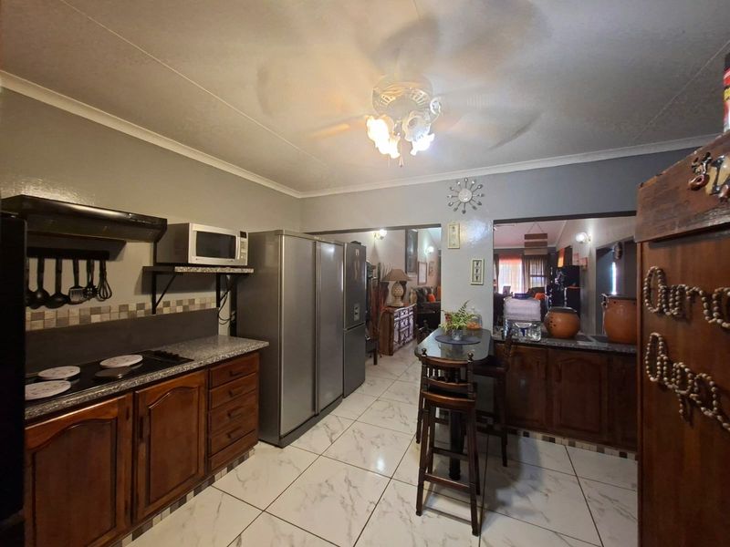 A functional kitchen featuring dark wood cabinetry, tiled flooring, a breakfast counter, and integrated appliances, opening into the adjacent living area.