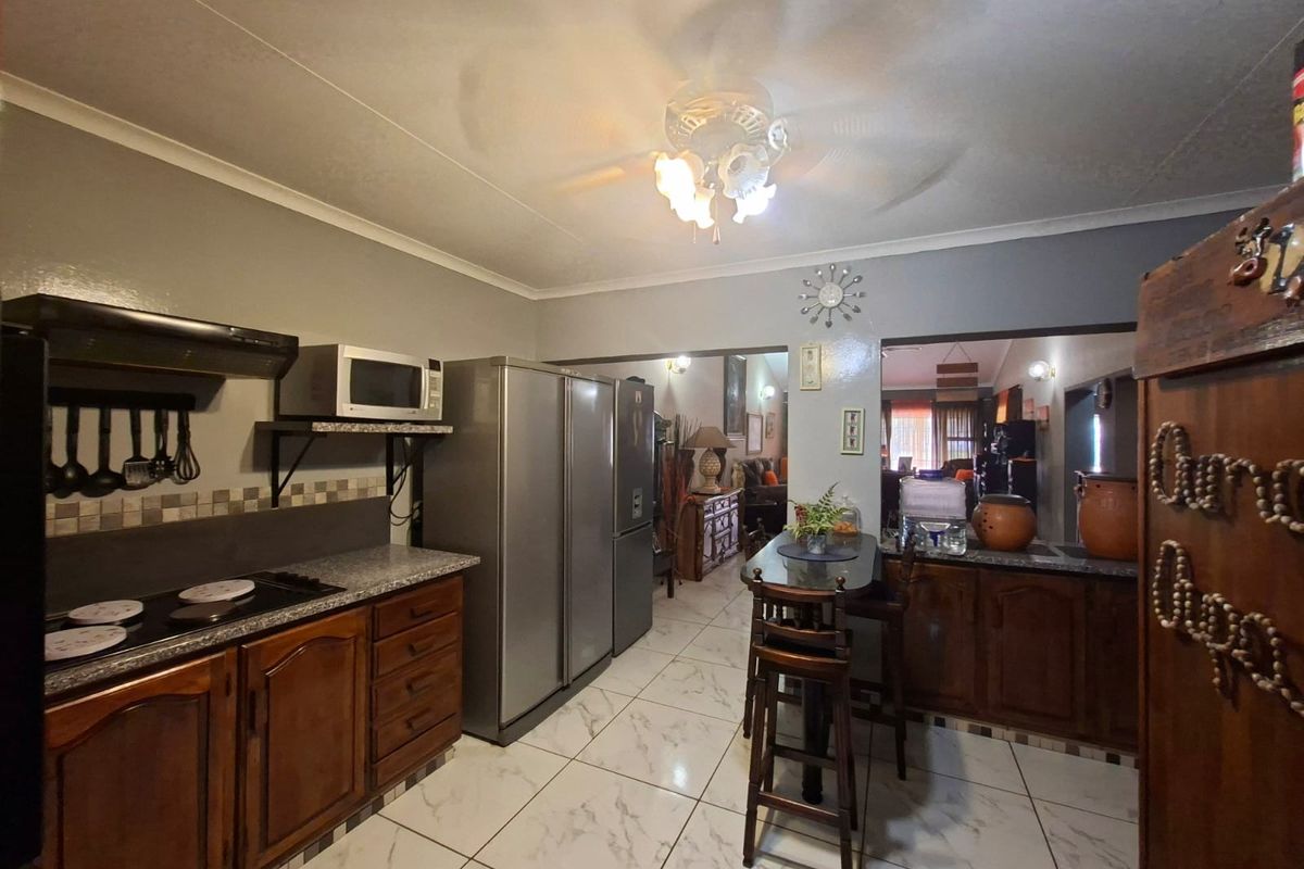 A functional kitchen featuring dark wood cabinetry, tiled flooring, a breakfast counter, and integrated appliances, opening into the adjacent living area.