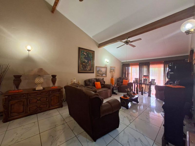 Spacious living room featuring vaulted ceilings with exposed timber beams, tiled flooring, and ample natural light through large windows.