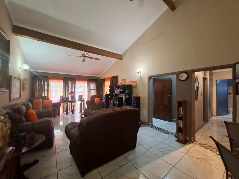 Spacious living room featuring a high vaulted ceiling with exposed timber beams, tiled flooring, and direct access to adjacent rooms.