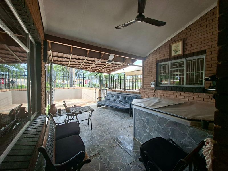 A covered outdoor patio area featuring tiled flooring, exposed brick walls, ceiling fans, and a built-in counter, ideal for outdoor entertaining.
