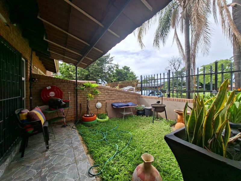 A covered patio area featuring tiled flooring, brick boundary walls, and metal security fencing, providing a functional outdoor space for relaxation.