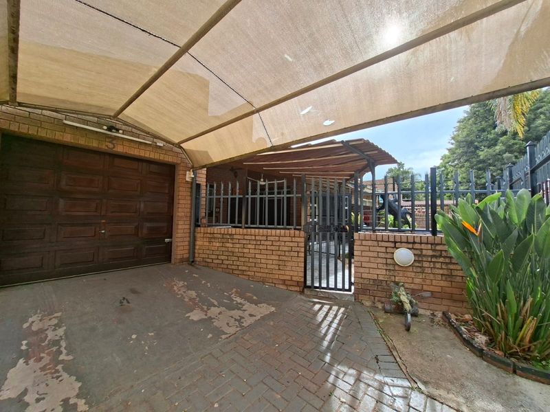 Front exterior view of the townhouse featuring a paved driveway, a covered carport with shade cloth, and a secure gated entrance.