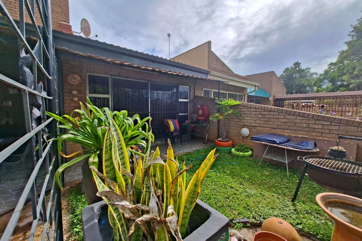 A private rear garden area featuring a small lawn, paved patio section, and brick boundary walls, accessible via a sliding glass door.