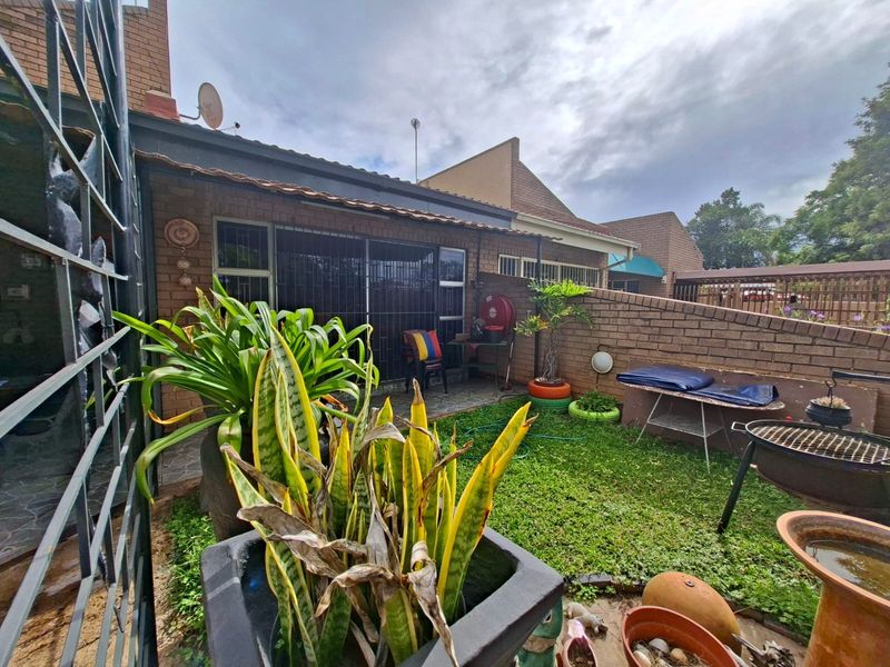A private rear garden area featuring a small lawn, paved patio section, and brick boundary walls, accessible via a sliding glass door.