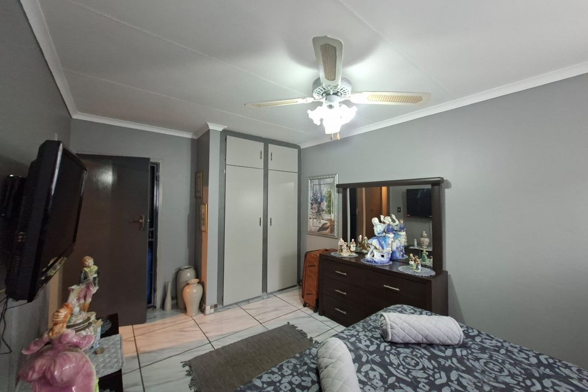 A bedroom featuring tiled flooring, built-in cupboards, and a ceiling fan, providing a functional space with neutral wall tones.