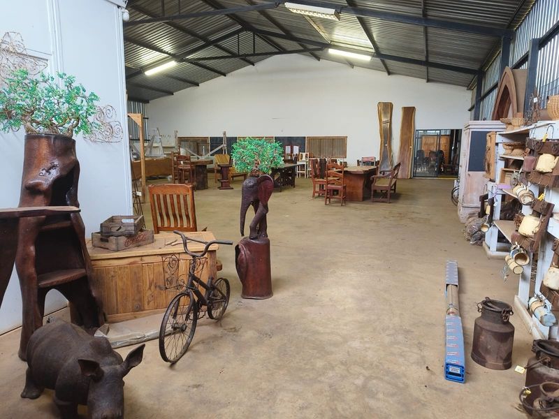 Large industrial-style utility space featuring exposed steel roof trusses, corrugated metal roofing, and concrete flooring, suitable for workshop or storage use.