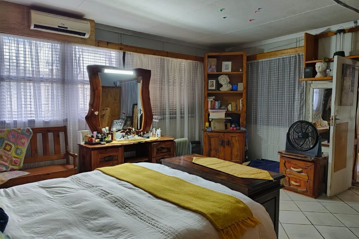 A bedroom featuring tiled flooring, a wall-mounted air conditioning unit, and built-in wooden shelving, requiring cosmetic updates to improve the overall finish.
