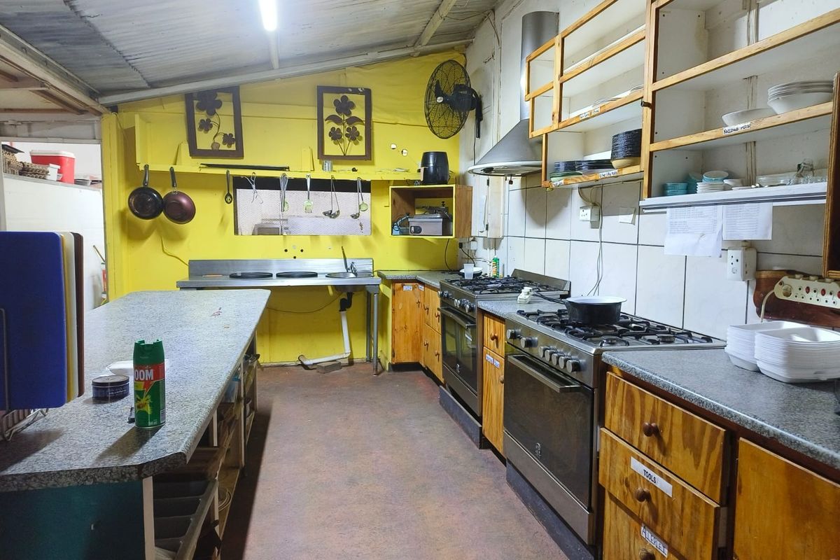 Functional kitchen area featuring a gas stove, extractor fan, stainless steel sink, and ample wooden cabinetry with laminate countertops.
