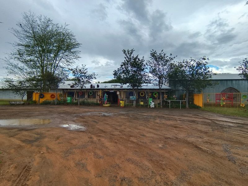 Front view of a small holding property featuring a rustic building structure with corrugated roofing and an expansive unpaved driveway area.