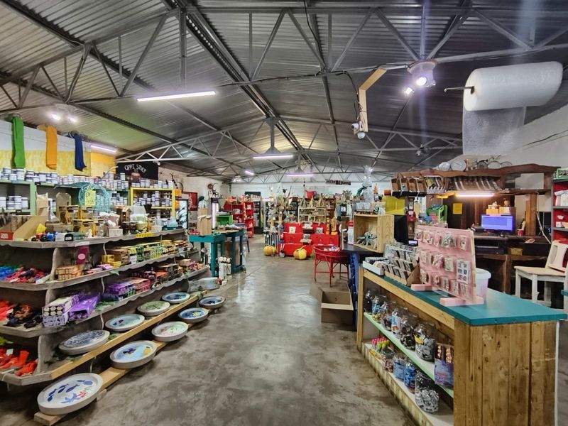 A spacious commercial utility area featuring exposed steel roof trusses, corrugated metal roofing, and durable concrete flooring, currently utilized as a retail space.