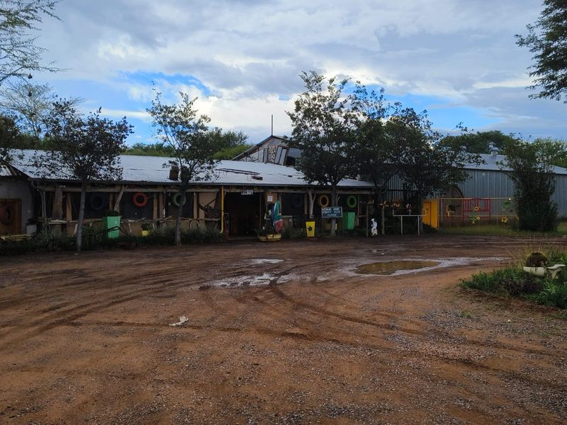 Front view of a small holding property featuring a rustic structure with a corrugated metal roof and an unpaved dirt driveway.
