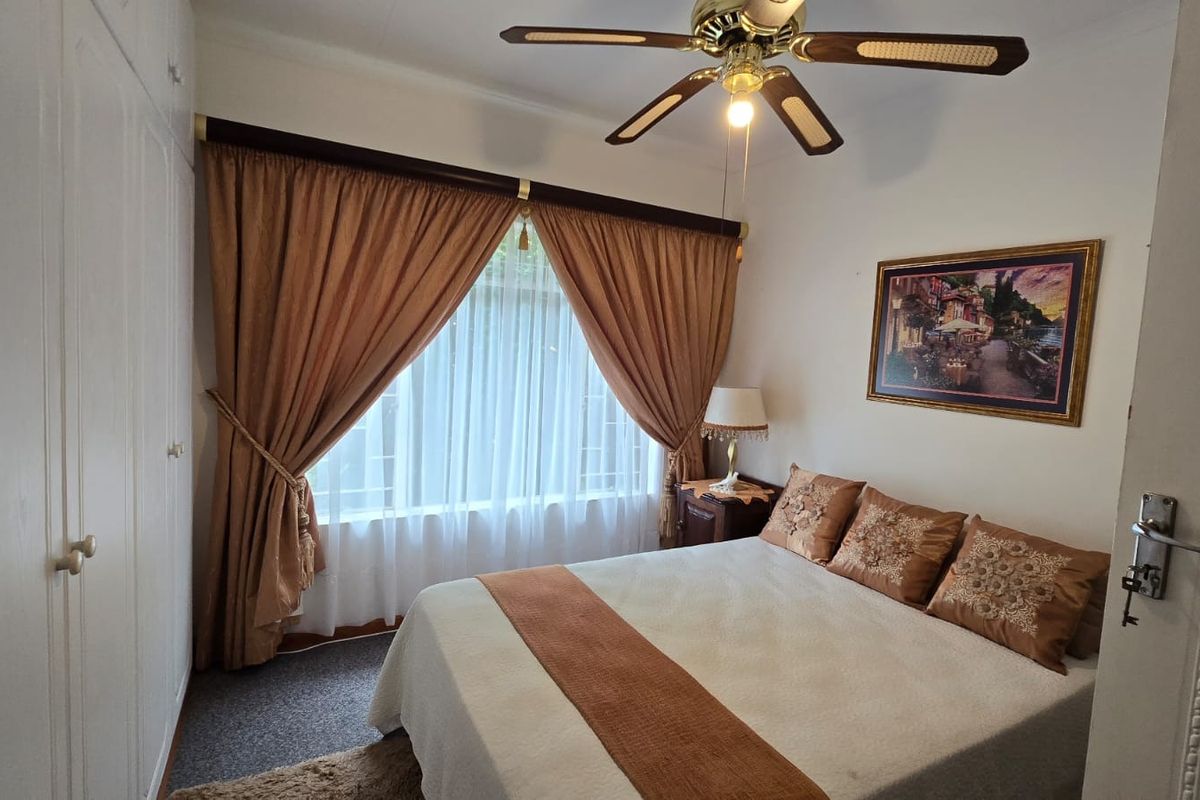 A cozy bedroom featuring built-in cupboards, a ceiling fan, and window security bars, offering a functional and comfortable living space.