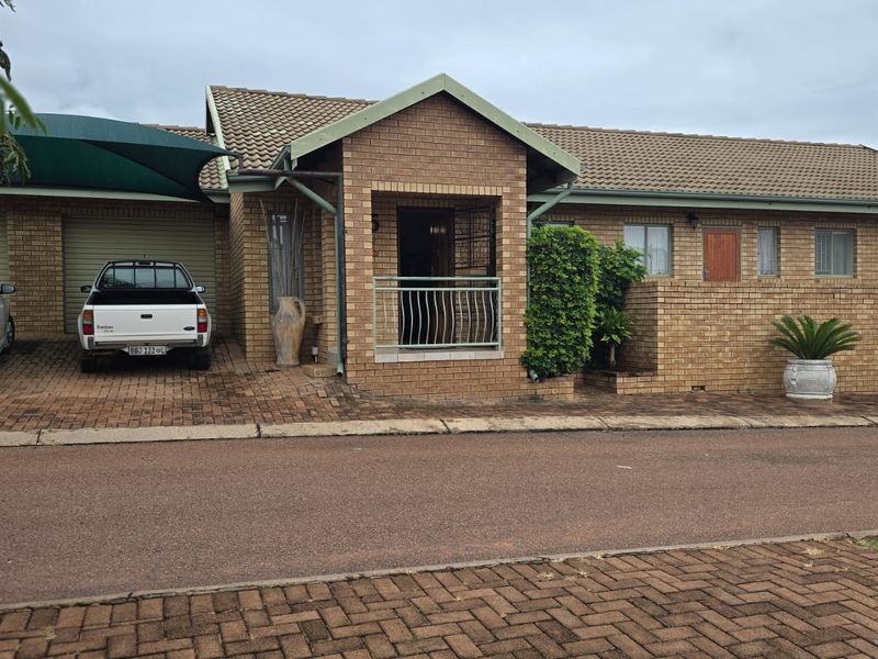 Front elevation of a face-brick house featuring a double garage, paved driveway, covered entrance, and established garden elements.