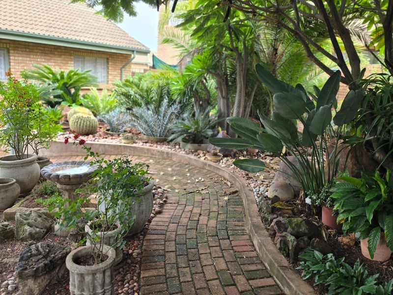 A well-maintained garden featuring a curved brick paved pathway, established landscaping, and mature trees alongside a brick residential exterior.