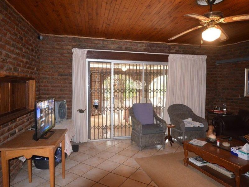 Living room featuring exposed brick walls, timber ceiling, tiled floors, and a sliding door leading to an outdoor area with security gate.
