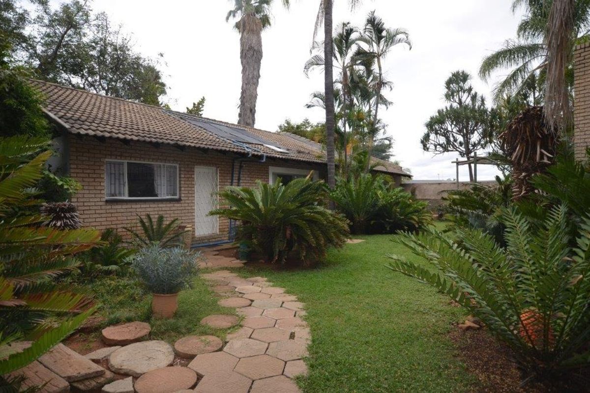 Rear view of a brick house featuring a tiled roof with solar panels, a paved garden path, and established landscaping.