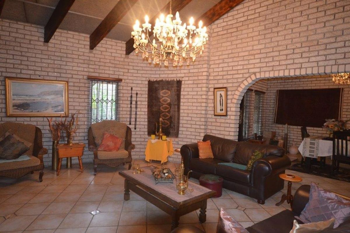 Spacious living room featuring exposed brick walls, timber ceiling beams, and ceramic tile flooring, with an arched transition to the adjacent dining area.