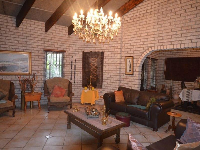 Spacious living room featuring exposed brick walls, timber ceiling beams, and ceramic tile flooring, with an arched transition to the adjacent dining area.