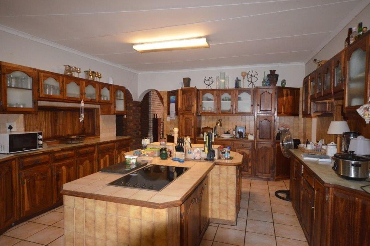 Spacious kitchen featuring extensive wooden cabinetry, tiled countertops with an integrated hob, and tiled flooring throughout.