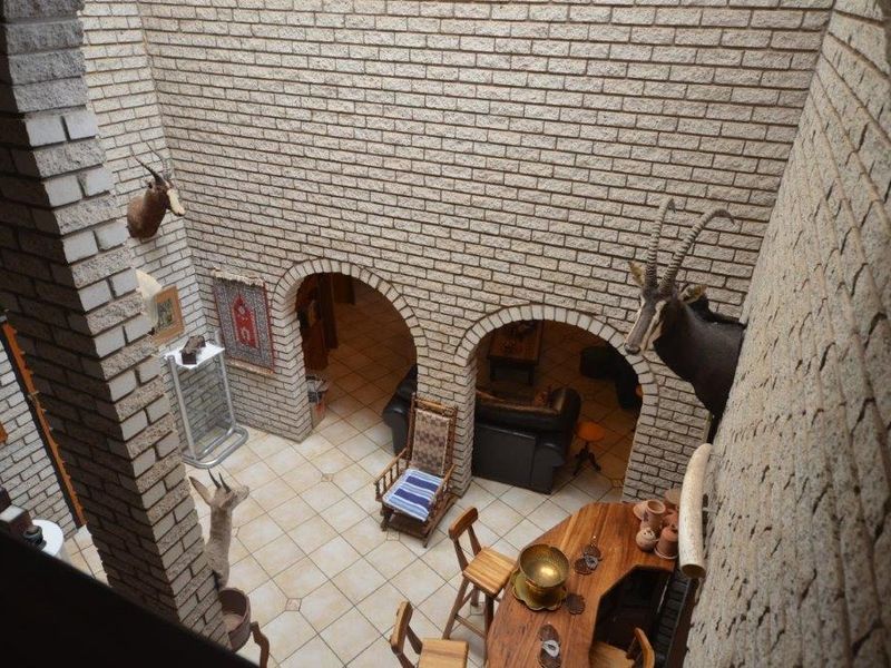 A double-volume living area featuring exposed brick walls, arched architectural details, and tiled flooring, viewed from an elevated mezzanine level.