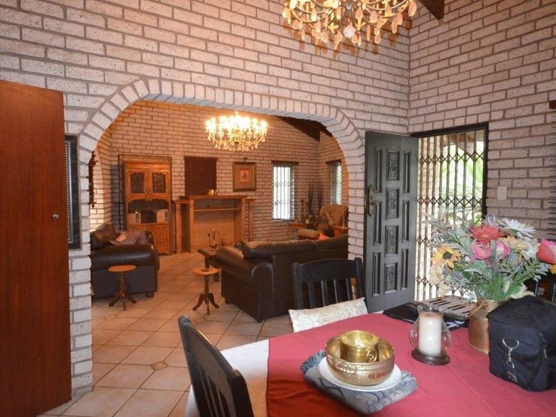 Open plan living and dining area featuring exposed brick walls, vaulted ceilings, an arched transition, and a built-in fireplace.