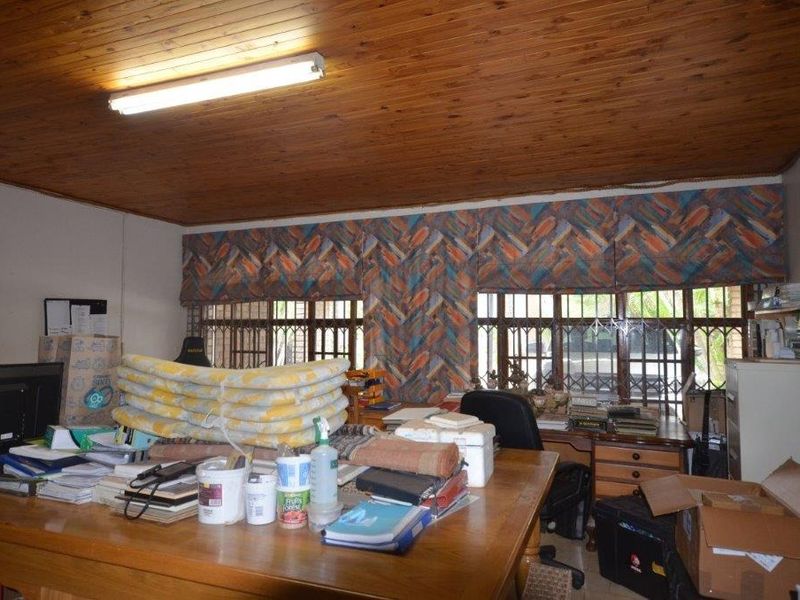 A functional office space featuring a timber-clad ceiling, large windows with security bars, and ample natural light.