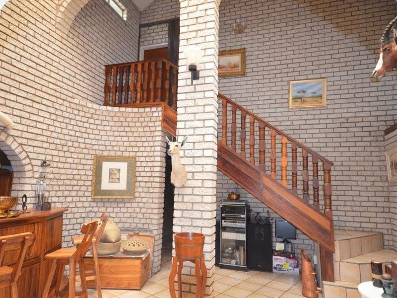 A double-volume entrance hall featuring exposed brickwork, a wooden staircase with a matching balustrade, and tiled flooring leading to a mezzanine level.