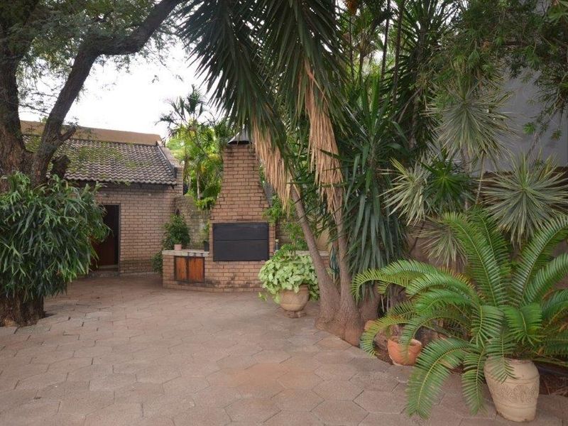 A private outdoor patio area featuring a built-in brick braai, paved flooring, and established garden surroundings.