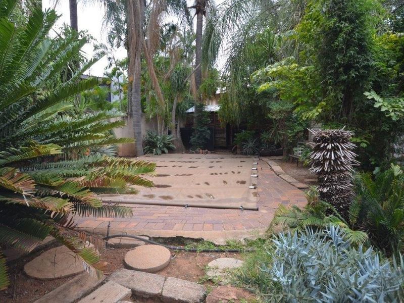 A private backyard pool area featuring a covered swimming pool surrounded by established garden landscaping and brick paving.