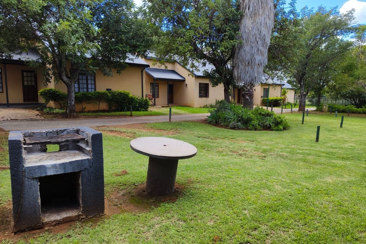 A well-maintained communal garden area featuring a built-in braai, paved pathways, and established trees, serving the adjacent residential units.