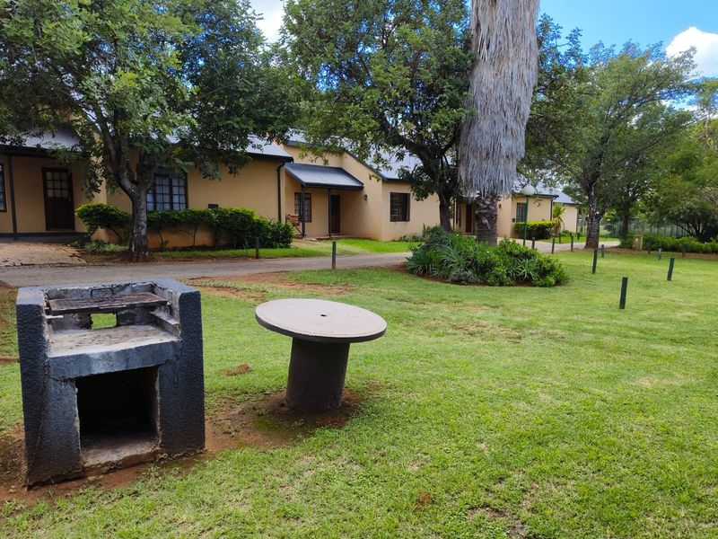 A well-maintained communal garden area featuring a built-in braai, paved pathways, and established trees, serving the adjacent residential units.