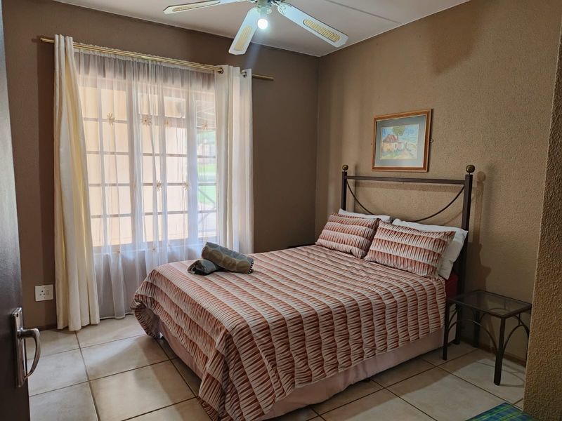 A cozy bedroom featuring tiled flooring, a ceiling fan, and a large window with natural light.