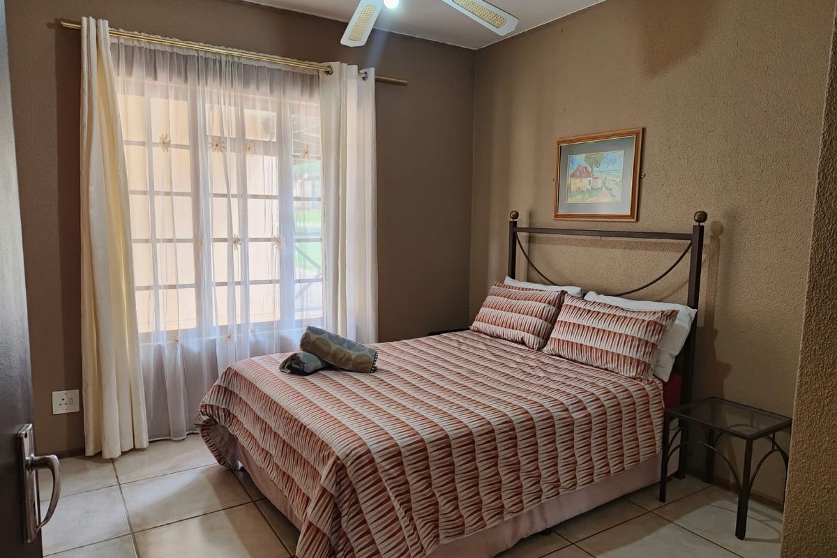 A cozy bedroom featuring tiled flooring, a ceiling fan, and a large window with natural light.